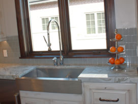 Stainless steel farm sink with white cabinetry in front of a large wood framed window.
