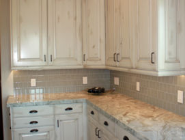White cabinetry with quartz counter top, tiled back splash and hardwood flooring.