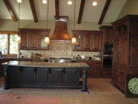 Wood kitchen cabinetry with black island and beautiful hammered copper hood