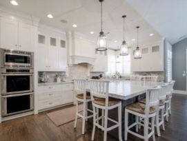 White kitchen cabinetry with gray island, back splash, counter tops and stainless appliances