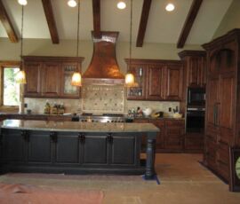 Wood kitchen cabinetry with black island and beautiful hammered copper hood