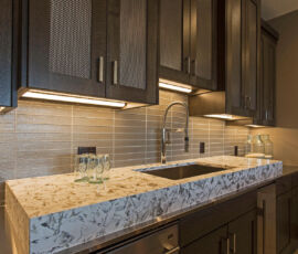 Wet bar with raised granite counter top and metal mesh in the top cabinets