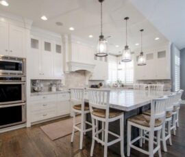 White kitchen cabinetry with gray island, back splash, counter tops and stainless appliances