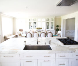White kitchen island with cook top and sink in front of white hutch